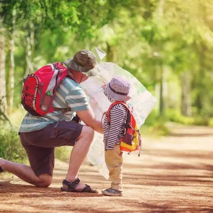 Father and boy going camping with tent in nature. Man with son with backpacks walking in the forest