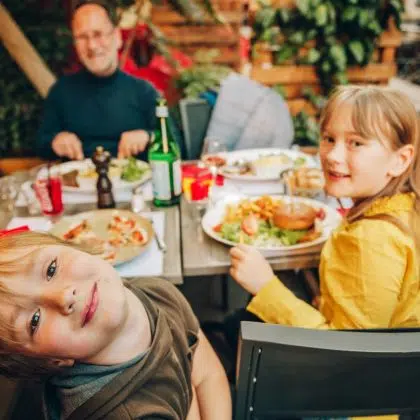 Happy family eating hamburger with french fries and pizza in outdoor restaurant